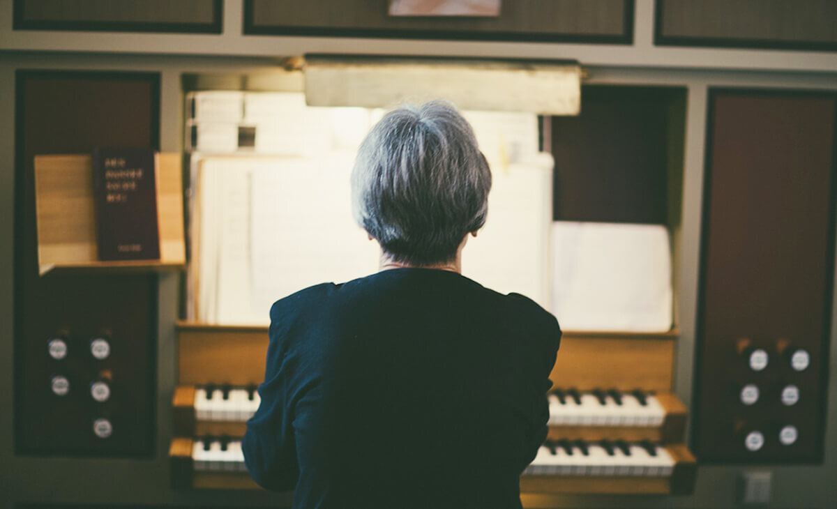 Back of an older persons head with a piano in the background